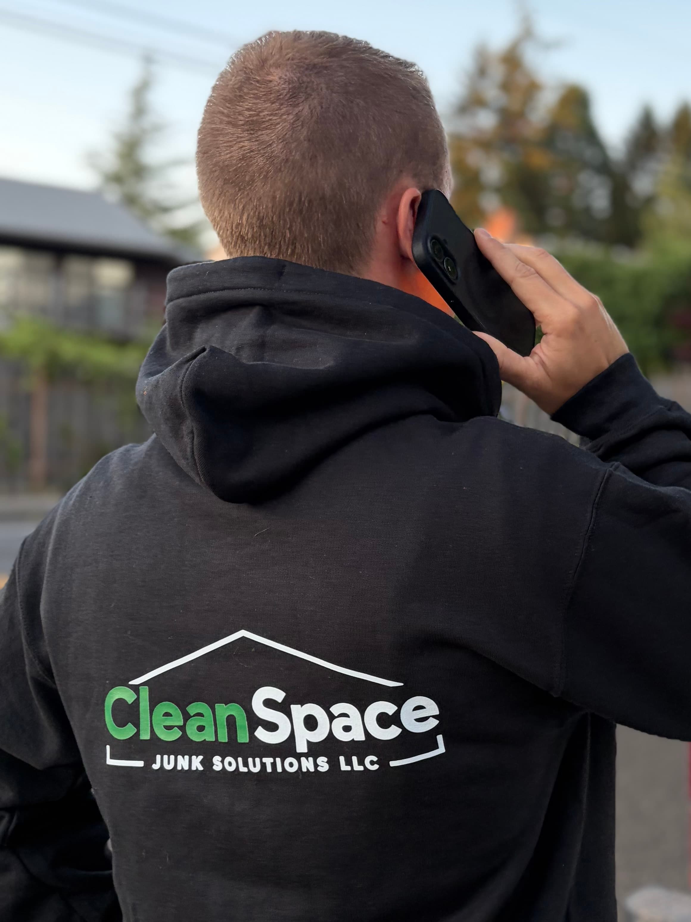 Man wearing a CleanSpace Junk Solutions LLC hoodie talking on a smartphone from behind.