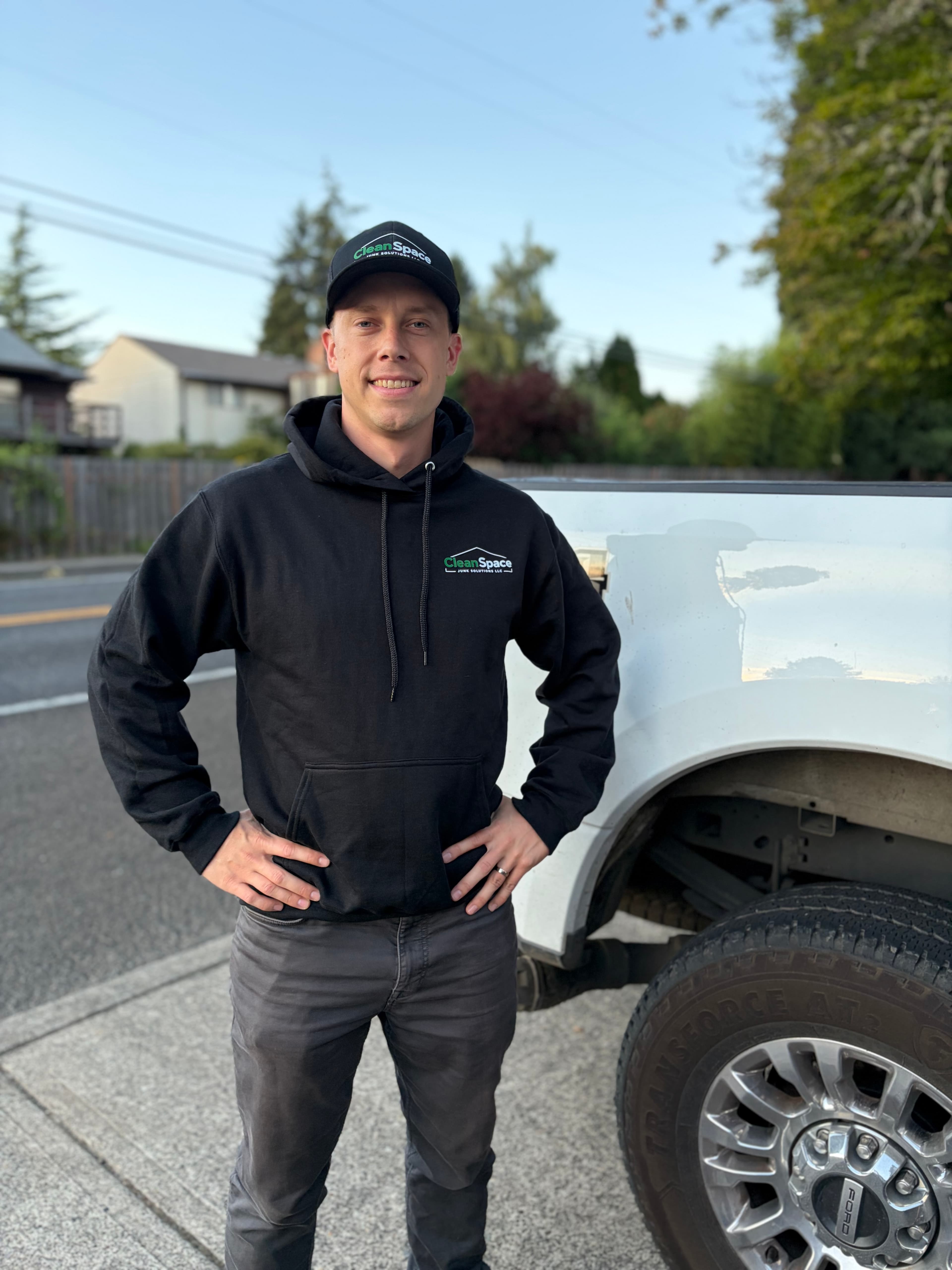 Smiling man in CleanSpace branded hoodie and cap stands beside a white pickup truck.