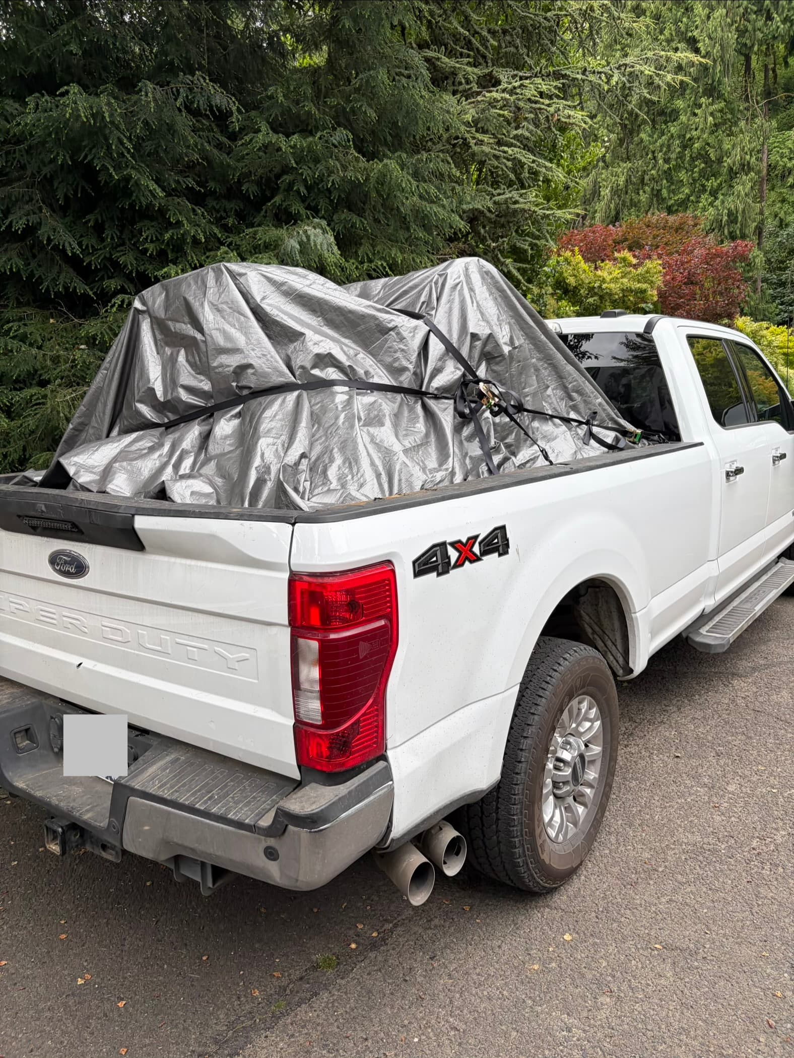 White Ford Super Duty pickup truck with bulky cargo covered by a silver tarp.