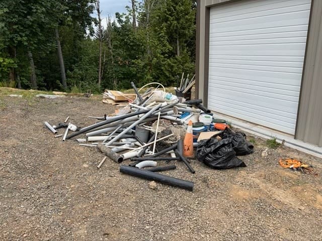 Pile of pipes, trash bags, and an orange cone next to a white garage door.
